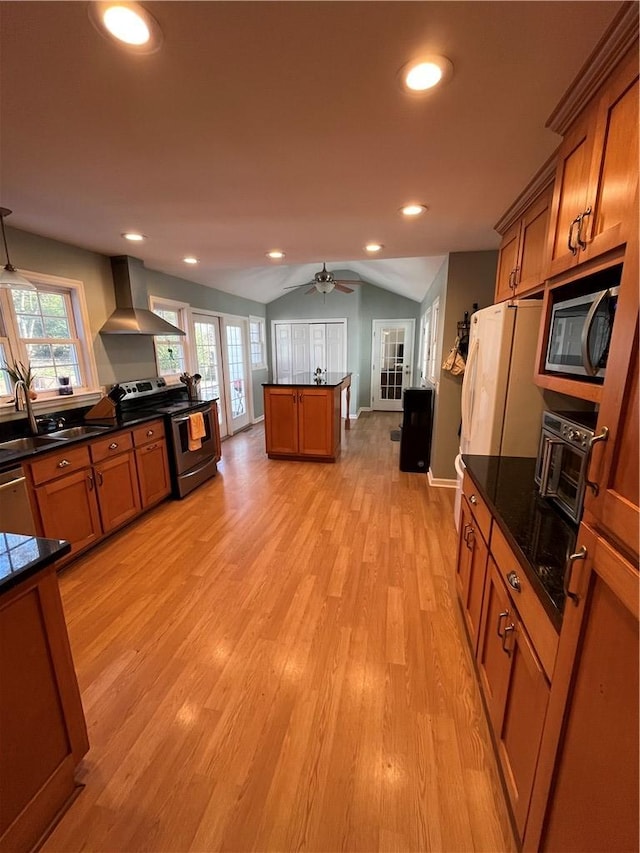 kitchen with wall chimney exhaust hood, sink, vaulted ceiling, light hardwood / wood-style flooring, and stainless steel appliances