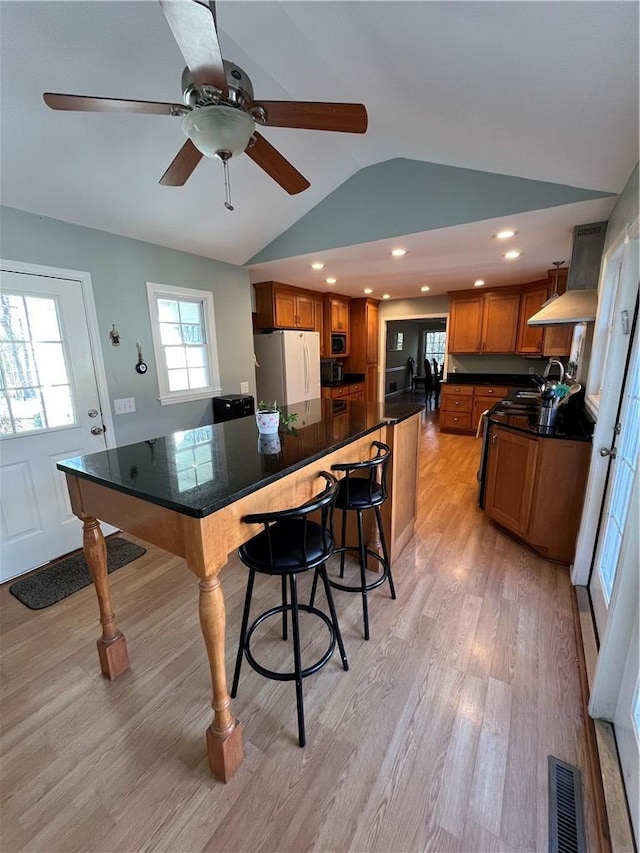 kitchen with vaulted ceiling, stainless steel microwave, a breakfast bar area, white fridge, and light wood-type flooring