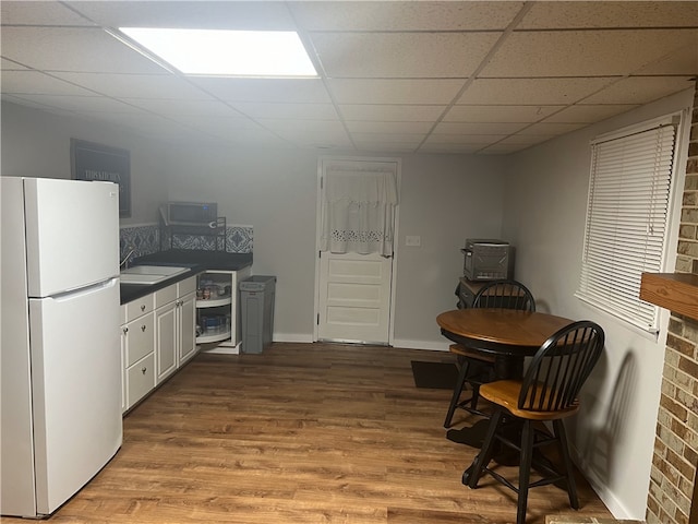 kitchen featuring sink, a paneled ceiling, white refrigerator, hardwood / wood-style flooring, and white cabinets