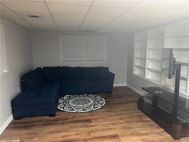 living room featuring wood-type flooring, built in features, and a drop ceiling