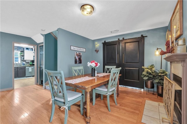 dining room with light wood-type flooring, a textured ceiling, baseboards, and a barn door