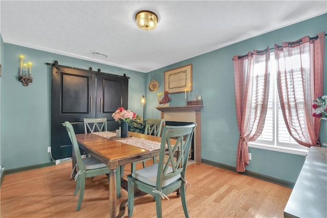 dining room featuring light wood-type flooring, visible vents, baseboards, and a barn door