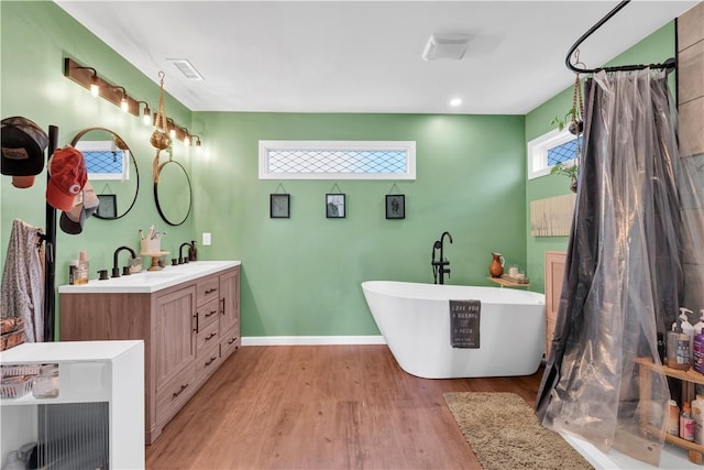 full bathroom featuring a freestanding tub, double vanity, a sink, and wood finished floors