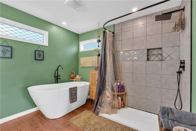 bathroom featuring recessed lighting, wood finished floors, baseboards, a freestanding bath, and a tile shower