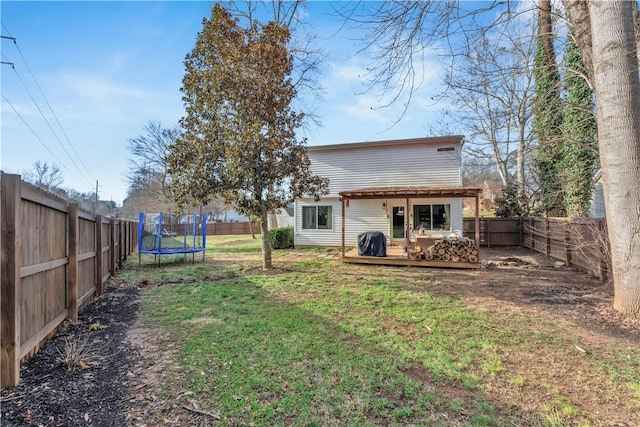 back of property featuring a deck, a trampoline, a fenced backyard, and a lawn