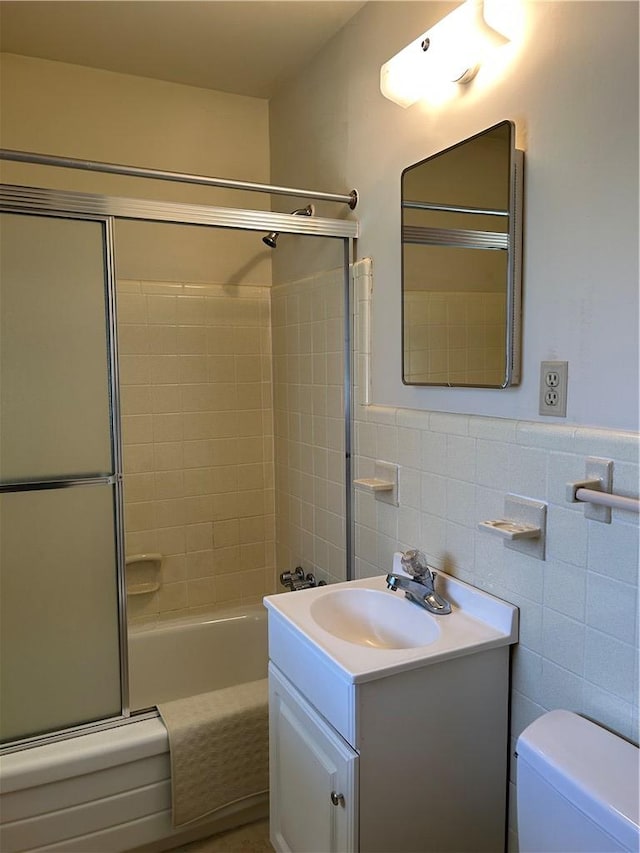 bathroom featuring bath / shower combo with glass door, toilet, a wainscoted wall, vanity, and tile walls