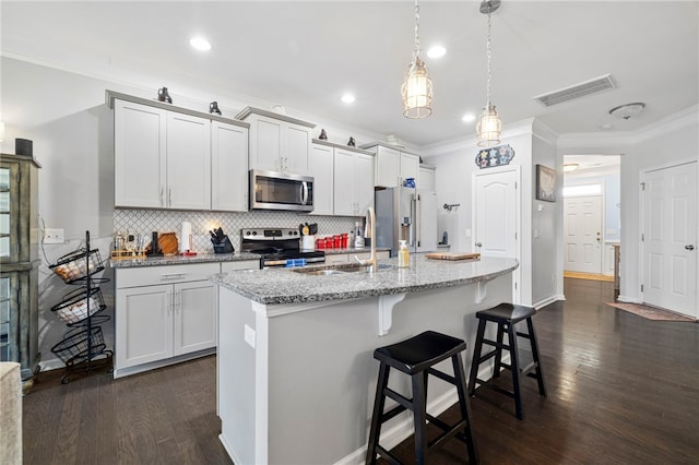 kitchen featuring appliances with stainless steel finishes, decorative light fixtures, light stone counters, and a center island with sink