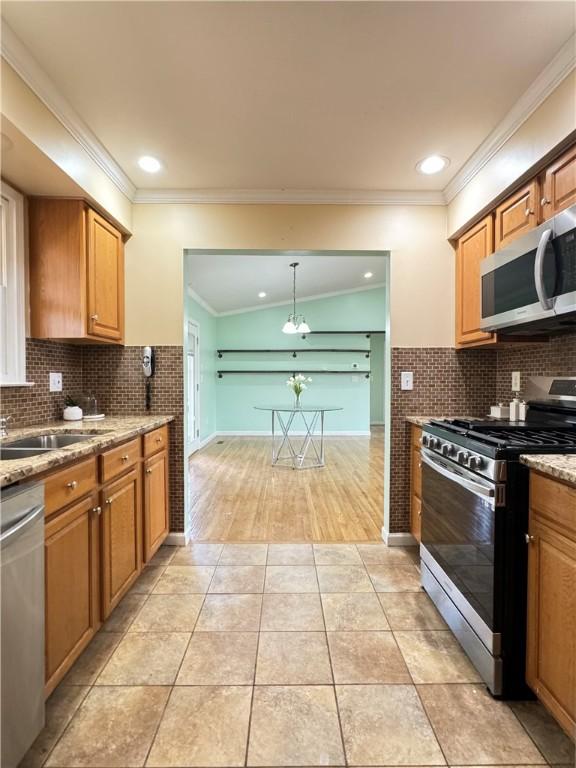 kitchen with appliances with stainless steel finishes, hanging light fixtures, light stone countertops, crown molding, and light tile patterned floors