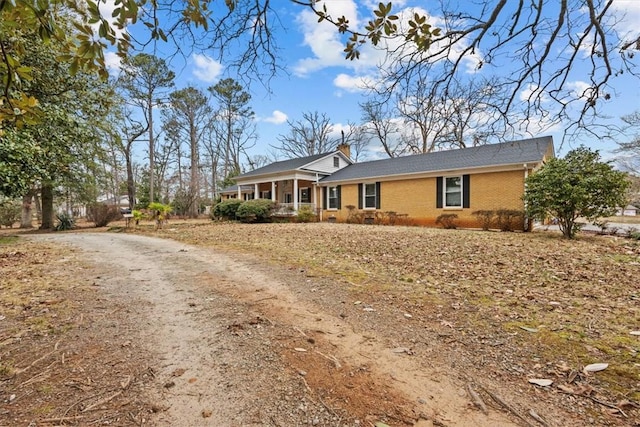 ranch-style house featuring dirt driveway, a chimney, and brick siding