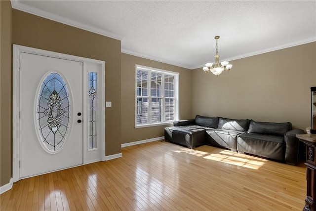 foyer with light hardwood / wood-style floors, crown molding, a textured ceiling, and an inviting chandelier