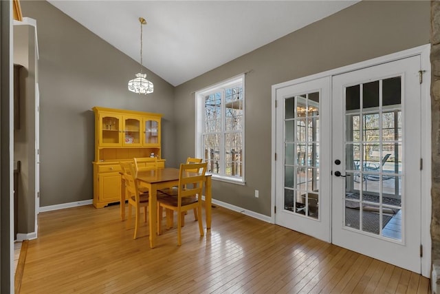 dining room with a notable chandelier, light hardwood / wood-style floors, vaulted ceiling, and french doors