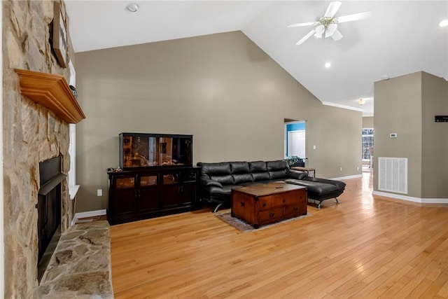 living room with ceiling fan, light hardwood / wood-style flooring, a stone fireplace, and high vaulted ceiling