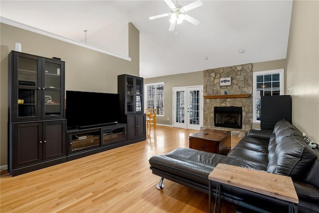 living room featuring a fireplace, french doors, light hardwood / wood-style floors, ceiling fan, and high vaulted ceiling