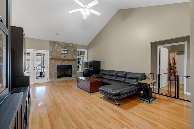 living room featuring light hardwood / wood-style flooring, a stone fireplace, high vaulted ceiling, and a healthy amount of sunlight