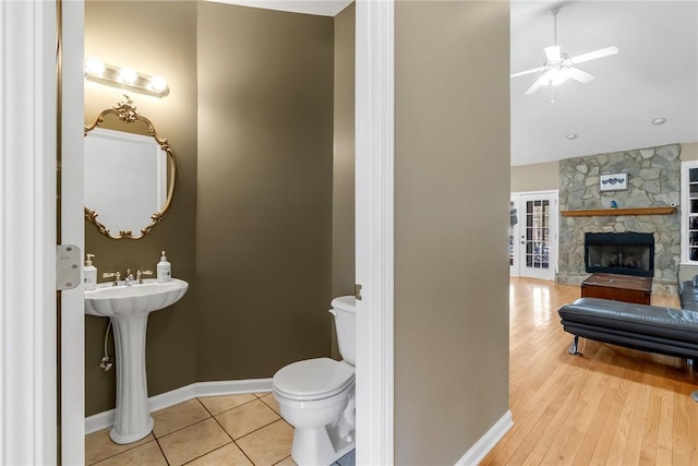 bathroom with ceiling fan, a stone fireplace, tile patterned flooring, and toilet