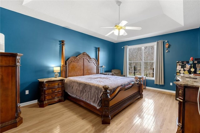 bedroom with light wood-type flooring, a tray ceiling, and ceiling fan