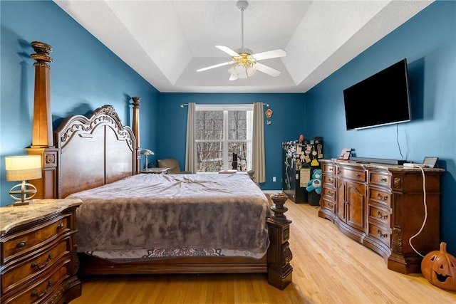 bedroom featuring a raised ceiling, light wood-type flooring, and ceiling fan