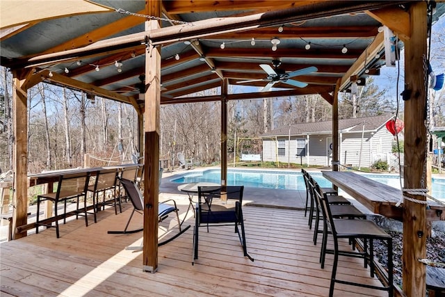 wooden terrace featuring exterior bar, ceiling fan, and an outdoor structure