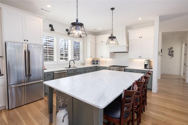 kitchen with appliances with stainless steel finishes, white cabinets, a center island, and decorative light fixtures