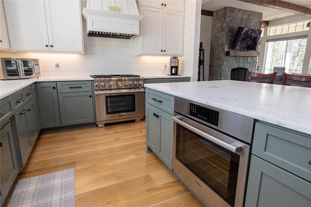 kitchen with light hardwood / wood-style flooring, premium range hood, stainless steel appliances, a fireplace, and white cabinetry