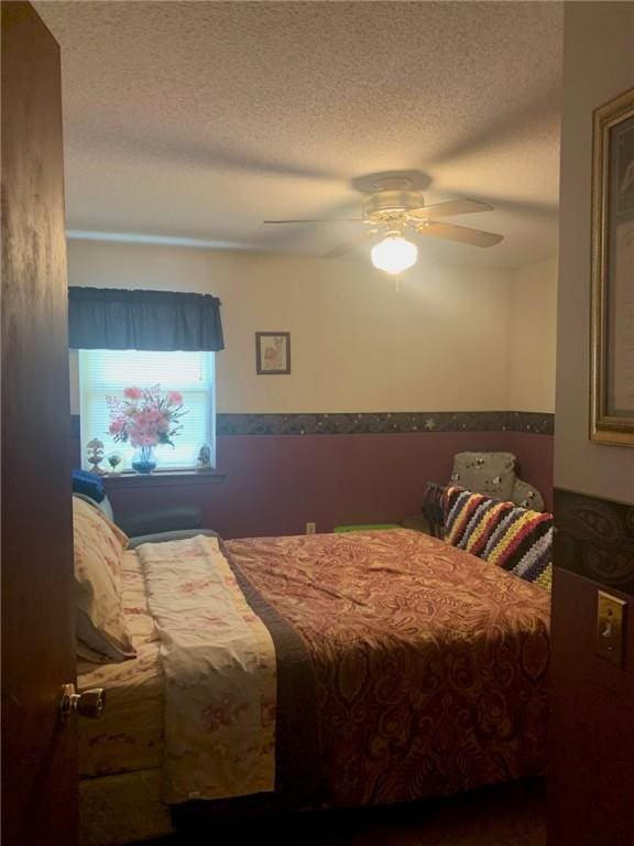 bedroom featuring ceiling fan, wainscoting, and a textured ceiling