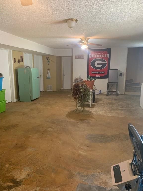 below grade area with freestanding refrigerator, a ceiling fan, a textured ceiling, and visible vents