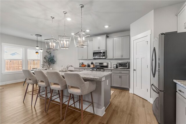 kitchen with a center island with sink, hanging light fixtures, a kitchen breakfast bar, stainless steel appliances, and light stone countertops