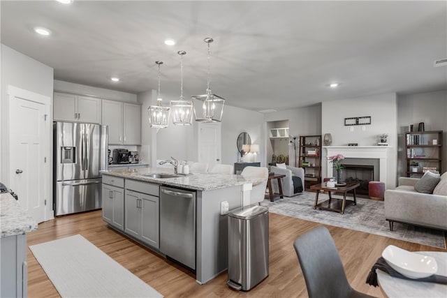 kitchen featuring gray cabinets, stainless steel appliances, a kitchen island with sink, and hanging light fixtures