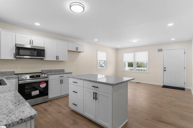 kitchen featuring stainless steel appliances, white cabinetry, light stone countertops, and a center island