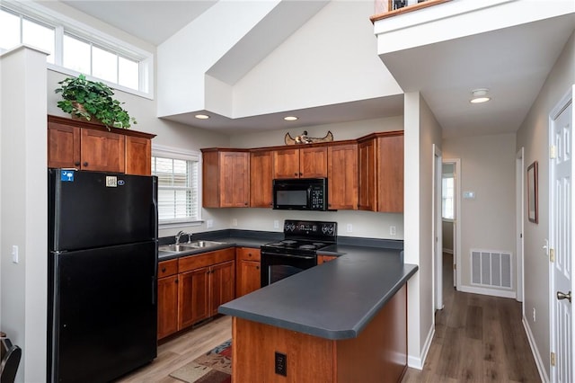 kitchen featuring kitchen peninsula, light hardwood / wood-style flooring, black appliances, a high ceiling, and sink