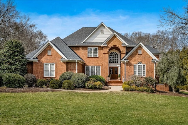 traditional-style house featuring roof with shingles, a front lawn, and brick siding