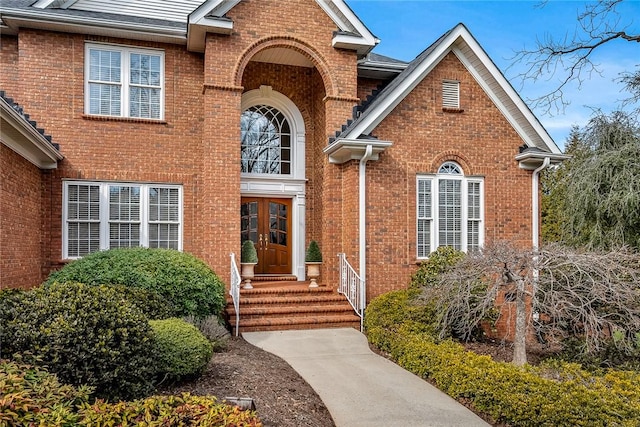 view of exterior entry with brick siding and a shingled roof