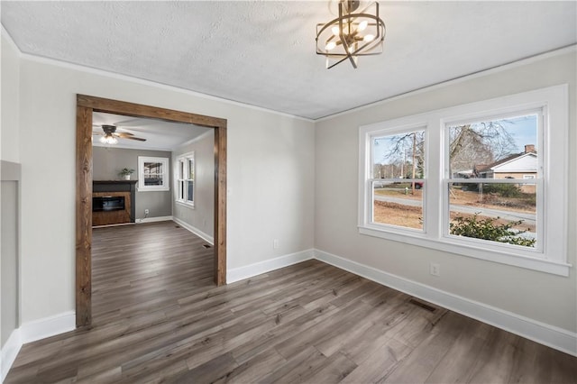 unfurnished dining area featuring a textured ceiling, dark wood-type flooring, baseboards, ornamental molding, and a glass covered fireplace