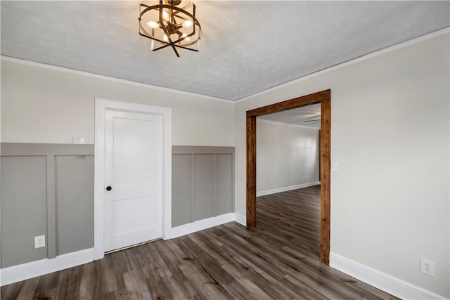 unfurnished room featuring dark wood-style floors, a notable chandelier, a decorative wall, ornamental molding, and a textured ceiling