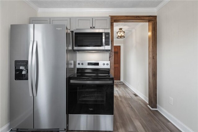 kitchen featuring dark wood-style floors, crown molding, gray cabinets, appliances with stainless steel finishes, and baseboards