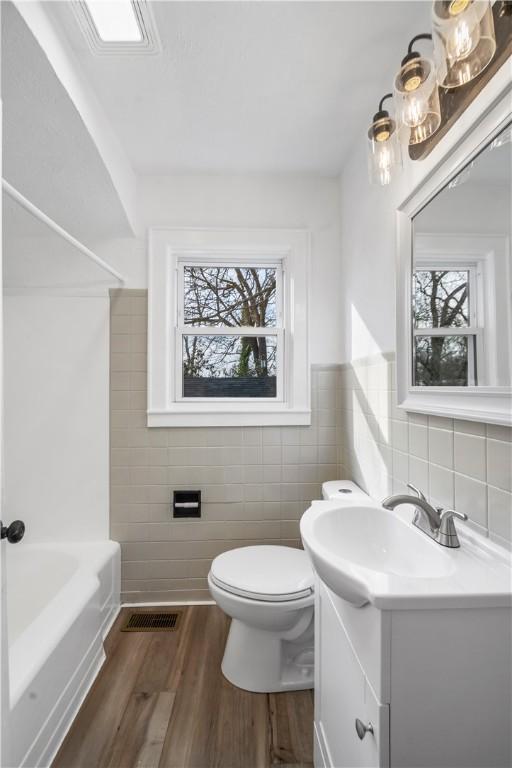 bathroom featuring visible vents, toilet, wood finished floors, vanity, and tile walls