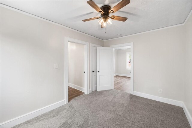 carpeted spare room featuring ceiling fan, baseboards, and crown molding