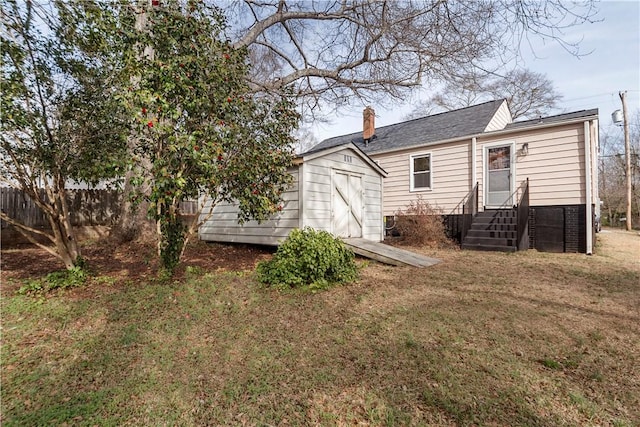 rear view of property featuring a yard, fence, a chimney, and a storage unit