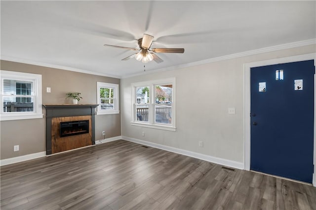 unfurnished living room with a ceiling fan, baseboards, dark wood finished floors, a glass covered fireplace, and crown molding