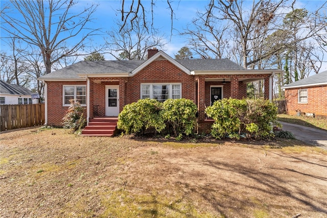 bungalow with brick siding, fence, a chimney, and roof with shingles