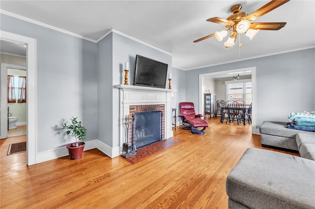 living area with crown molding, a fireplace, light wood-style flooring, ceiling fan, and baseboards