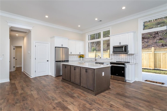 kitchen with tasteful backsplash, a kitchen island, stainless steel appliances, light countertops, and white cabinetry