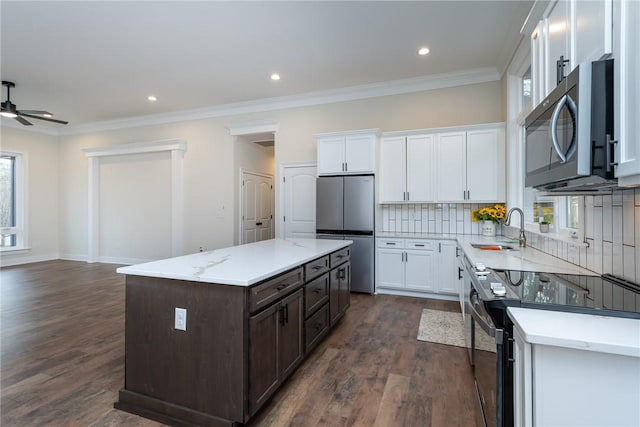 kitchen with a center island, a sink, stainless steel appliances, white cabinetry, and backsplash