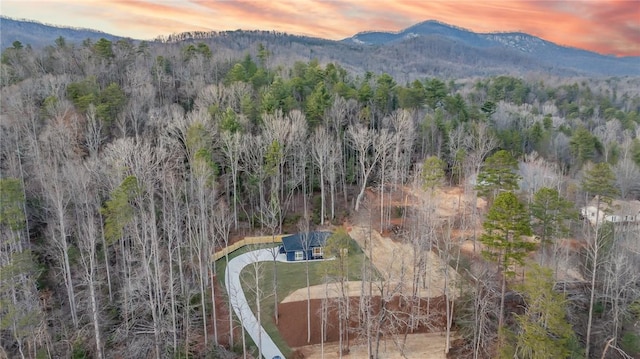 aerial view at dusk featuring a wooded view and a mountain view