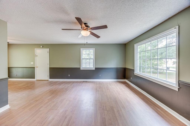 unfurnished room with a textured ceiling, wainscoting, ceiling fan, and light wood-type flooring