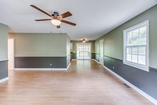 empty room featuring a textured ceiling, light wood-style flooring, visible vents, baseboards, and a ceiling fan