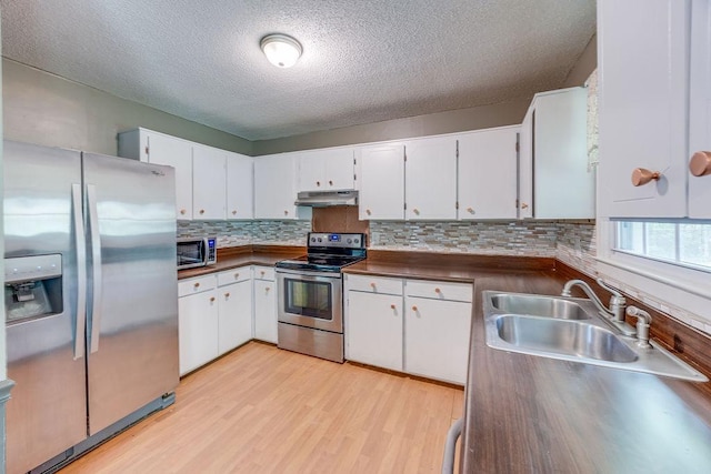 kitchen with under cabinet range hood, stainless steel appliances, a sink, white cabinetry, and dark countertops