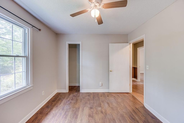 unfurnished bedroom featuring ceiling fan, a textured ceiling, baseboards, and wood finished floors