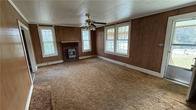 unfurnished living room featuring carpet floors, wood walls, a brick fireplace, and heating unit