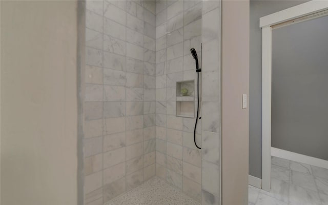 bathroom with marble finish floor, tiled shower, and baseboards